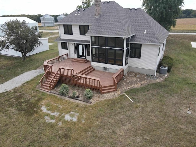 rear view of property featuring a deck, a shingled roof, a yard, a sunroom, and a chimney