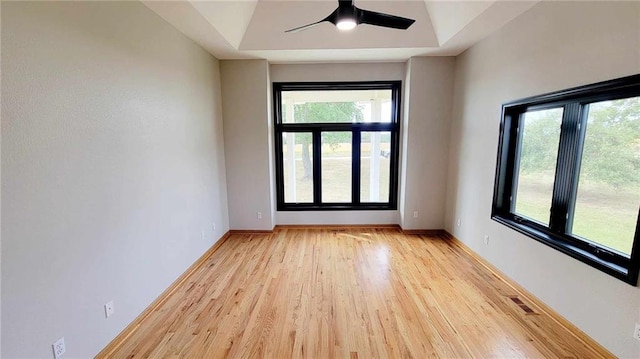 spare room featuring baseboards, a raised ceiling, light wood-style flooring, and a ceiling fan