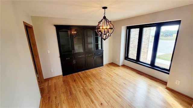 unfurnished dining area with an inviting chandelier, light wood-style flooring, and baseboards