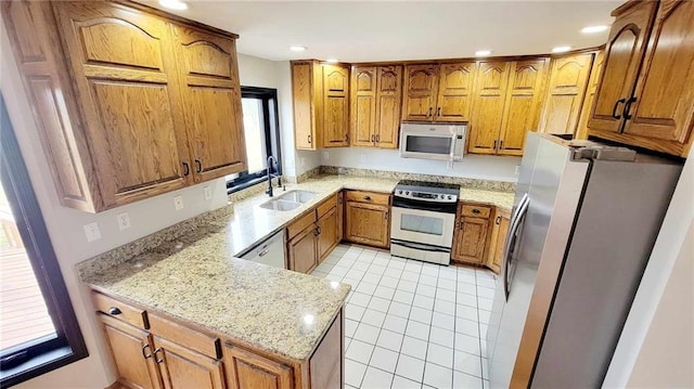 kitchen featuring light tile patterned floors, a peninsula, a sink, appliances with stainless steel finishes, and brown cabinets