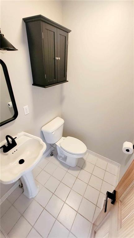 bathroom featuring tile patterned flooring, toilet, baseboards, and a sink