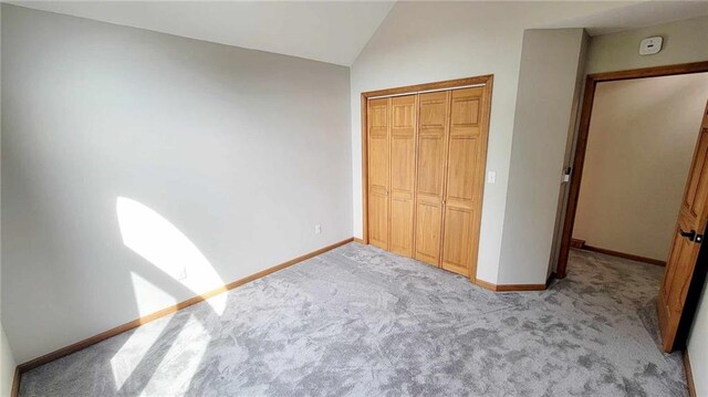 unfurnished bedroom with lofted ceiling, light colored carpet, baseboards, and a closet