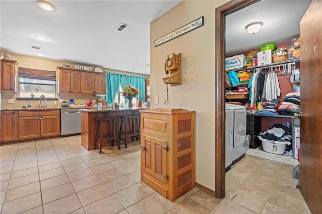 kitchen featuring visible vents, washing machine and dryer, brown cabinets, stainless steel dishwasher, and a sink