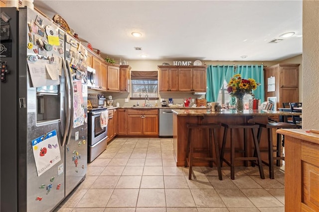 kitchen featuring light tile patterned floors, brown cabinetry, a kitchen island, a breakfast bar, and appliances with stainless steel finishes