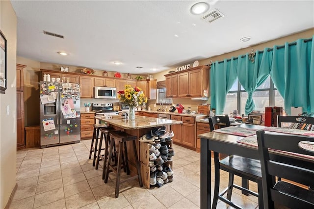kitchen featuring a kitchen breakfast bar, visible vents, appliances with stainless steel finishes, and brown cabinets