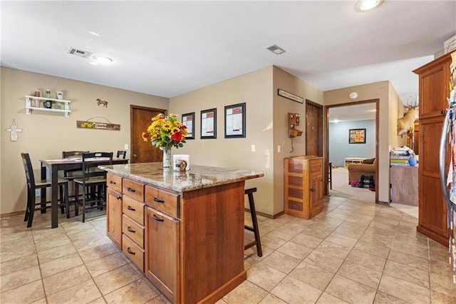 kitchen with visible vents, a center island, a kitchen bar, light stone counters, and brown cabinets