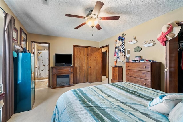 bedroom with ensuite bathroom, a textured ceiling, a glass covered fireplace, light colored carpet, and ceiling fan