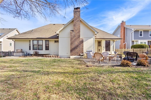 back of property featuring fence, a yard, roof with shingles, a chimney, and a patio area