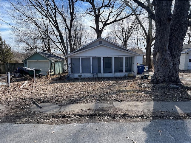 bungalow-style house featuring fence, a detached garage, an outdoor structure, and a sunroom