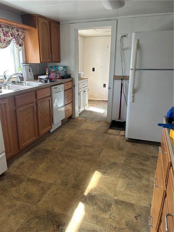 kitchen featuring brown cabinetry, stone finish floor, white appliances, and a sink