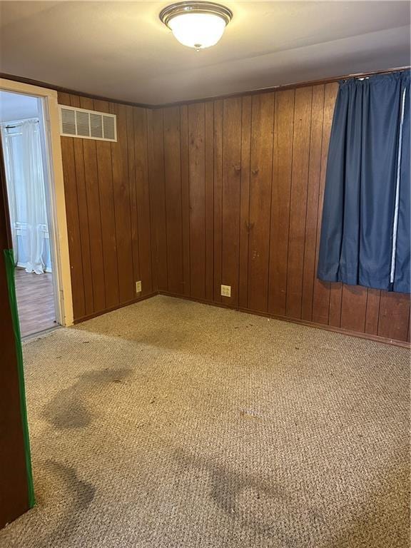 spare room with light carpet, visible vents, and wood walls