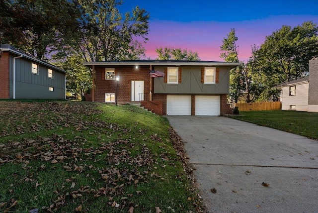 raised ranch featuring brick siding, an attached garage, concrete driveway, and a front yard