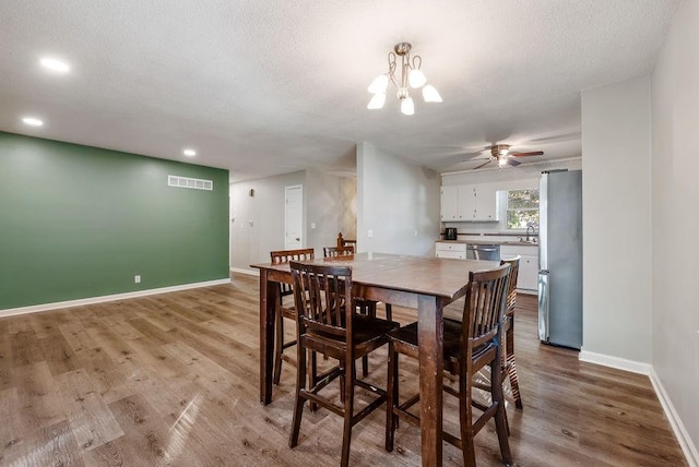 dining room featuring visible vents, a textured ceiling, baseboards, and wood finished floors