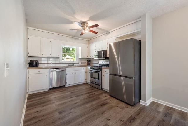 kitchen featuring ceiling fan, dark wood finished floors, appliances with stainless steel finishes, white cabinets, and a sink