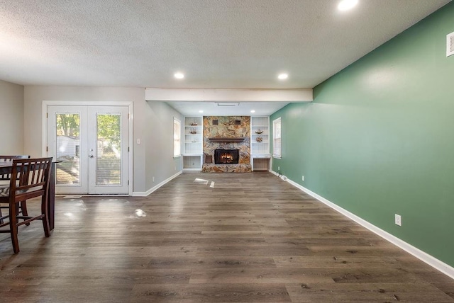 living room with baseboards, dark wood-type flooring, a stone fireplace, and a textured ceiling