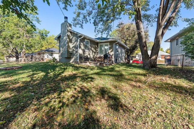 rear view of house with a lawn, french doors, entry steps, and fence