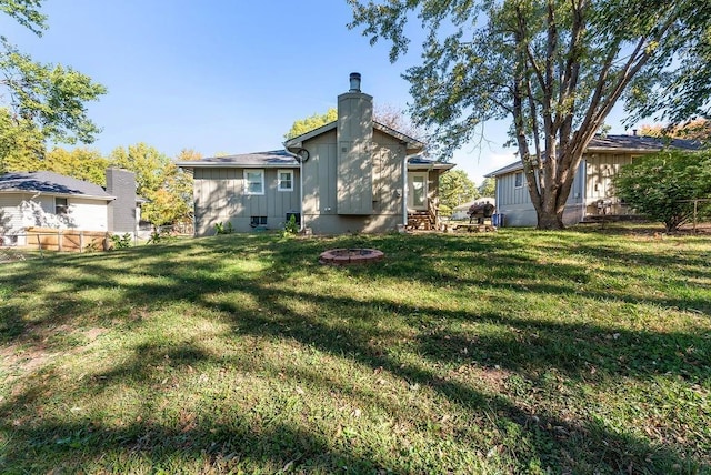 back of house featuring an outdoor fire pit, a chimney, a yard, and fence