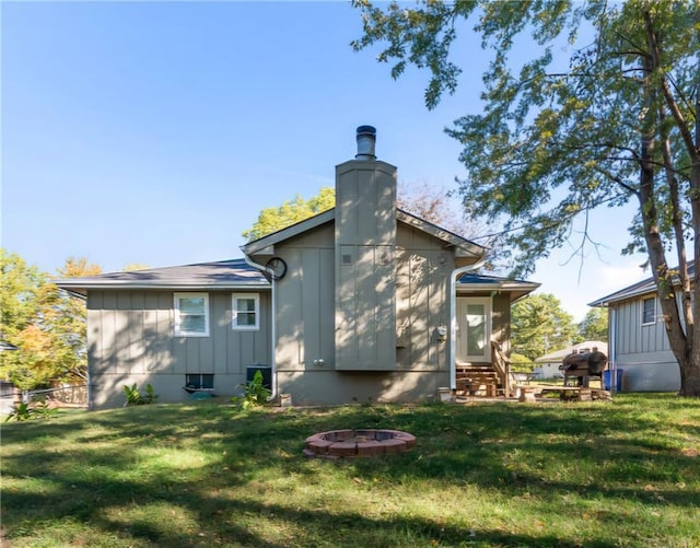 rear view of property with board and batten siding, entry steps, an outdoor fire pit, a lawn, and a chimney