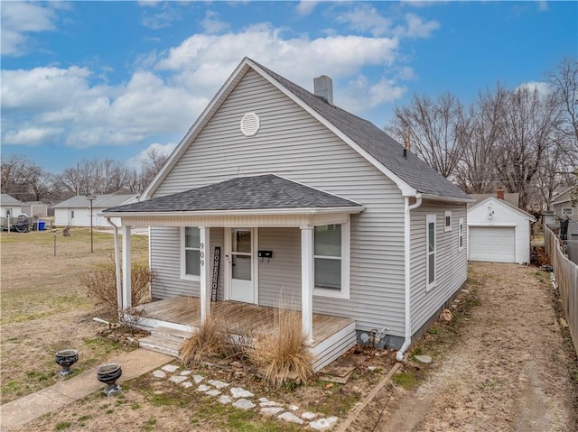 bungalow featuring a detached garage, fence, roof with shingles, covered porch, and an outdoor structure