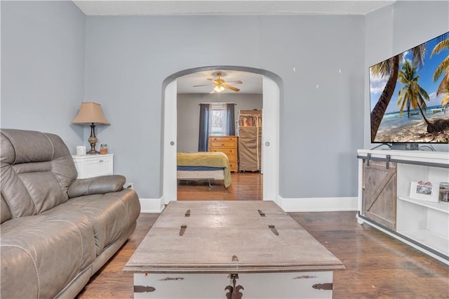 living room featuring ceiling fan, baseboards, arched walkways, and wood finished floors