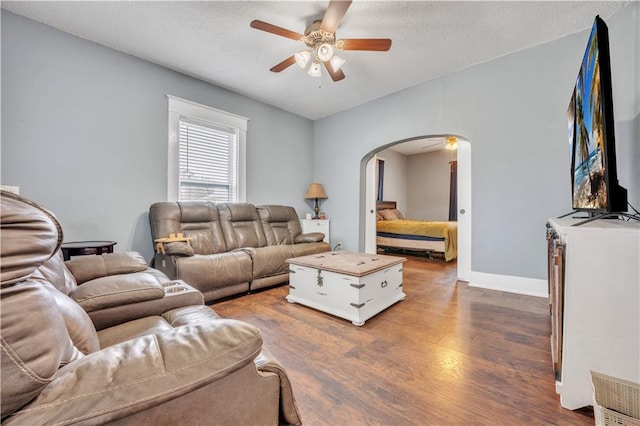 living area with baseboards, ceiling fan, arched walkways, a textured ceiling, and dark wood-style flooring