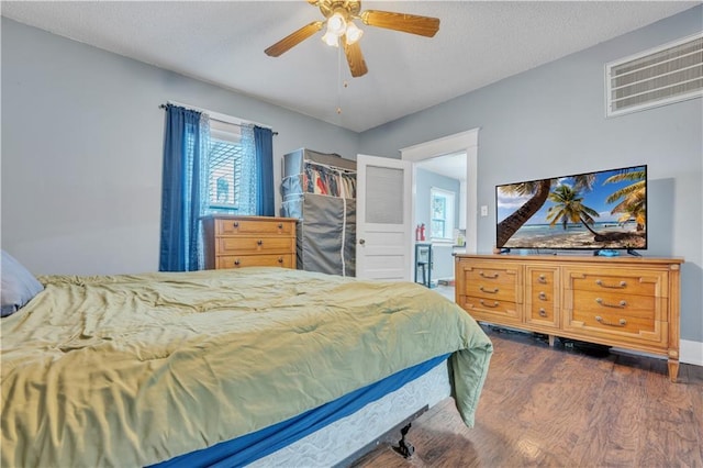 bedroom with dark wood-style floors, visible vents, a textured ceiling, and ceiling fan