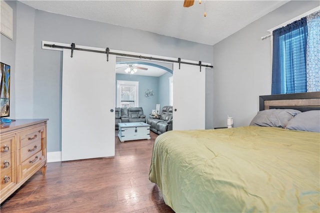 bedroom featuring ceiling fan, a barn door, dark wood-type flooring, and a textured ceiling