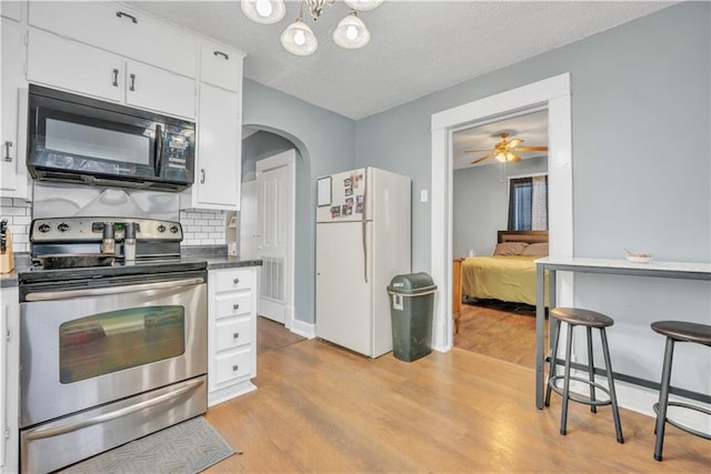 kitchen featuring black microwave, light wood-style flooring, stainless steel electric range, freestanding refrigerator, and arched walkways