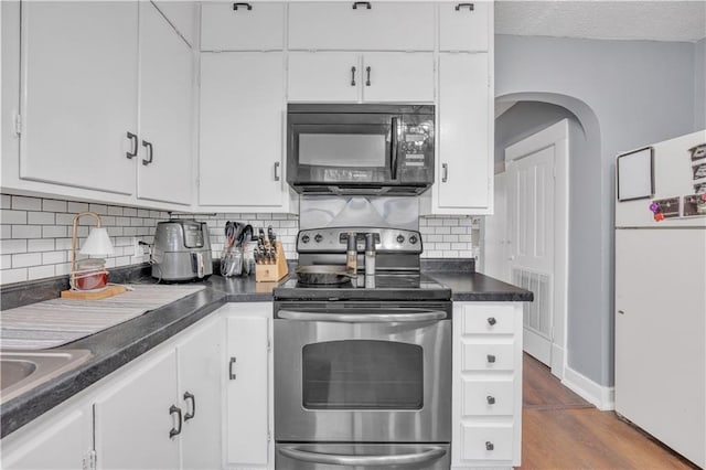 kitchen featuring visible vents, freestanding refrigerator, electric stove, black microwave, and white cabinetry