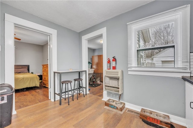 interior space featuring visible vents, heating unit, a textured ceiling, wood finished floors, and baseboards