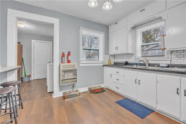 kitchen with heating unit, wood finished floors, a sink, decorative backsplash, and dark countertops