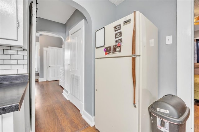 kitchen with wood finished floors, arched walkways, freestanding refrigerator, decorative backsplash, and white cabinetry