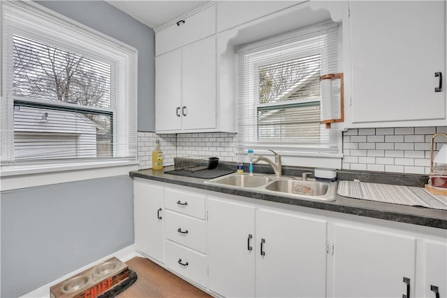 kitchen with dark countertops, white cabinets, backsplash, and a sink