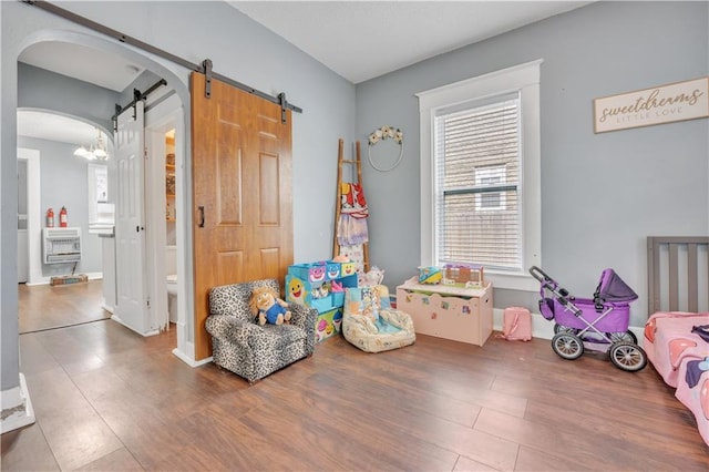 game room with heating unit, wood finished floors, baseboards, arched walkways, and a barn door