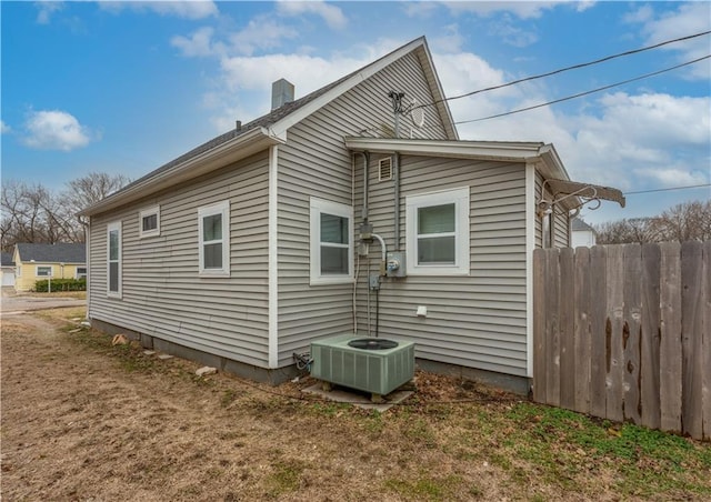 view of property exterior featuring a chimney, central AC, and fence