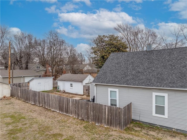 back of property featuring an outbuilding, roof with shingles, and fence