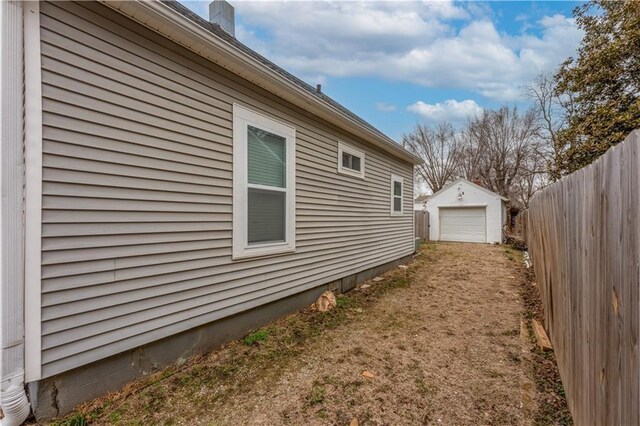 view of side of home featuring an outbuilding, driveway, a detached garage, fence, and a chimney