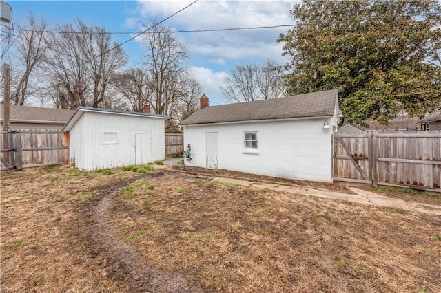 back of house featuring concrete block siding, an outdoor structure, a gate, and a fenced backyard