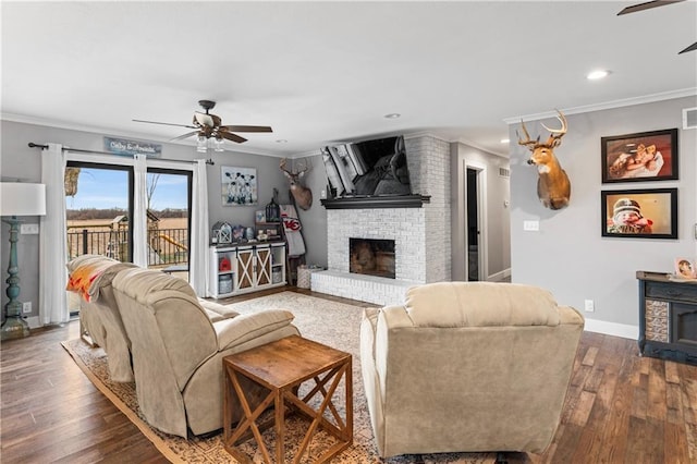 living area featuring hardwood / wood-style floors, a ceiling fan, baseboards, crown molding, and a brick fireplace