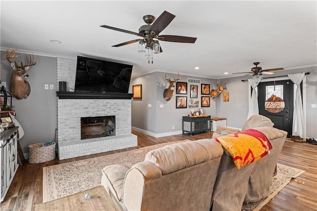 living area with visible vents, a brick fireplace, baseboards, ornamental molding, and wood finished floors