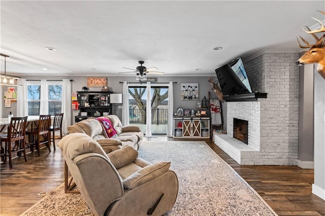 living area featuring a fireplace, crown molding, ceiling fan, and wood finished floors