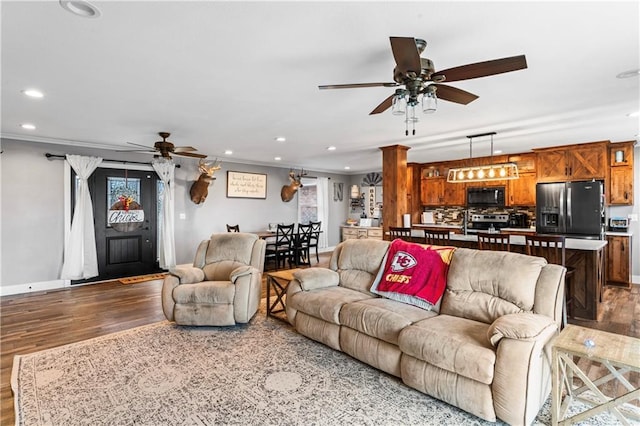 living area with wood finished floors, recessed lighting, crown molding, baseboards, and ceiling fan