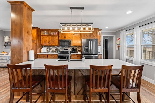 kitchen with brown cabinets, a sink, backsplash, stainless steel appliances, and crown molding