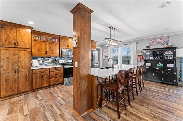 kitchen with wood finished floors, a sink, decorative backsplash, appliances with stainless steel finishes, and brown cabinets