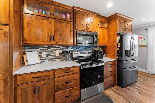 kitchen with stainless steel appliances, light countertops, crown molding, brown cabinets, and backsplash