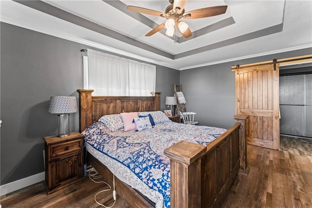 bedroom featuring dark wood-style floors, baseboards, a tray ceiling, a barn door, and crown molding