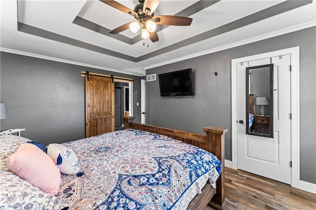 bedroom featuring wood finished floors, a barn door, baseboards, crown molding, and a raised ceiling