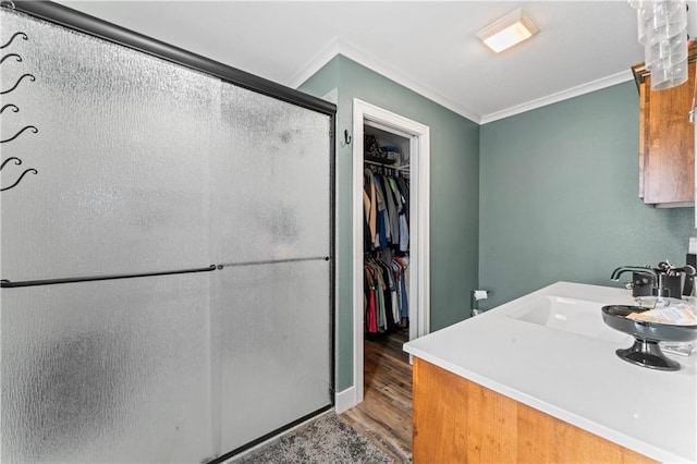 bathroom featuring a spacious closet, crown molding, a stall shower, wood finished floors, and a sink