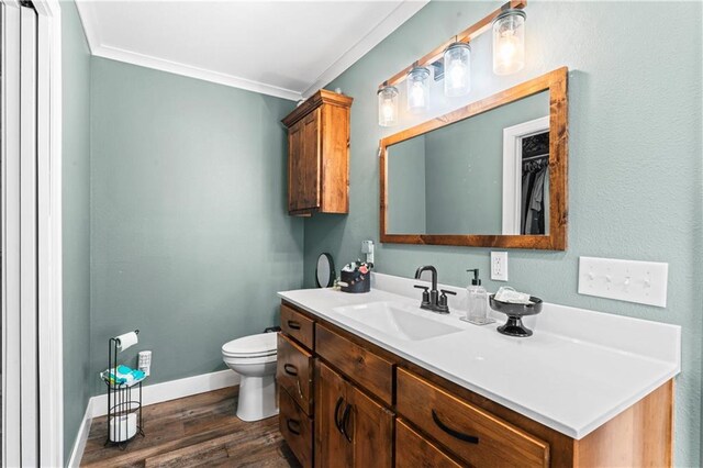 bathroom with vanity, wood finished floors, baseboards, crown molding, and toilet