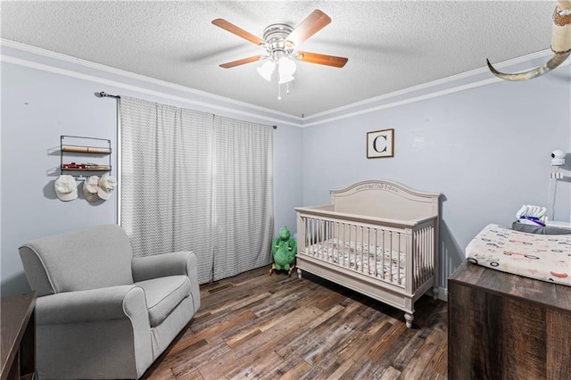 bedroom featuring a crib, a ceiling fan, a textured ceiling, wood finished floors, and crown molding